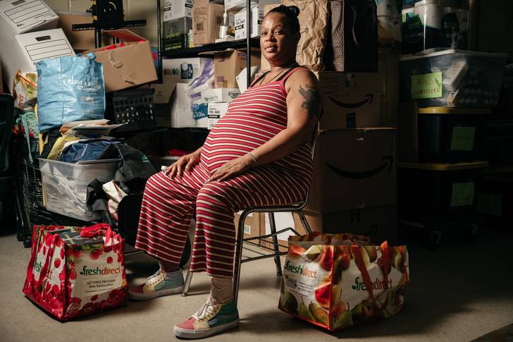 A woman, who is pregnant, sits in front of boxes in an office in her public housing complex.
